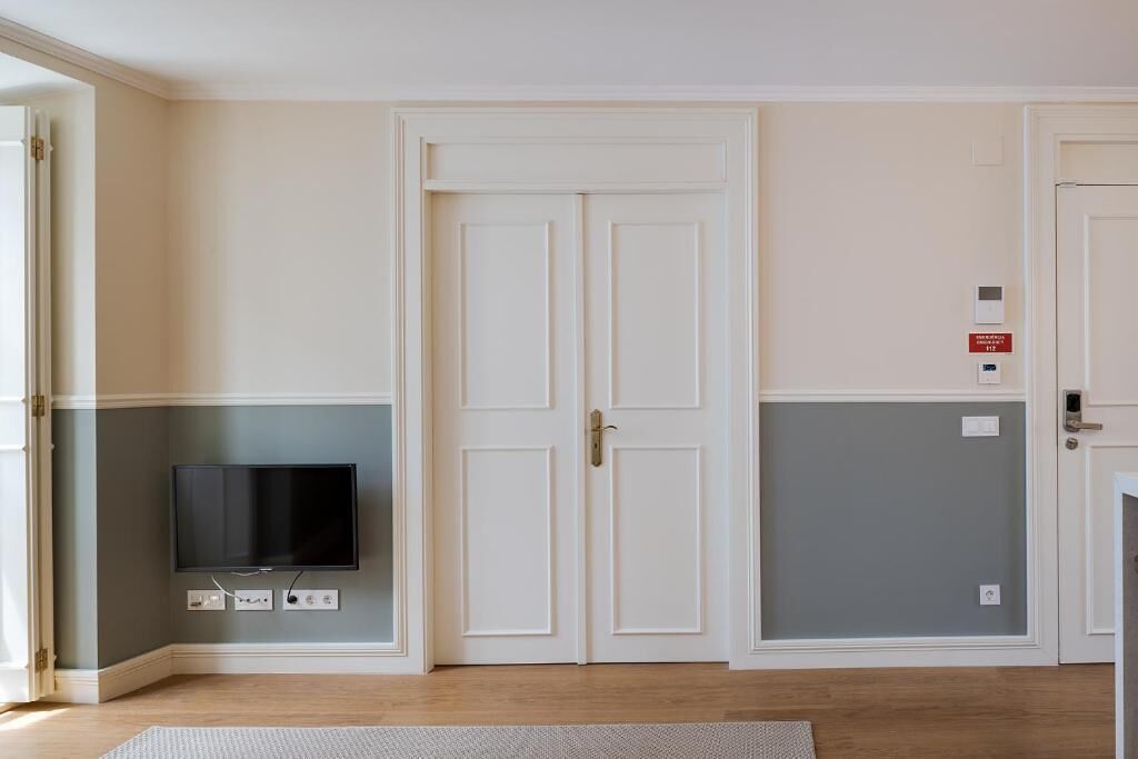 A room with a television mounted on the wall, a double door, and a light switch on the wall.