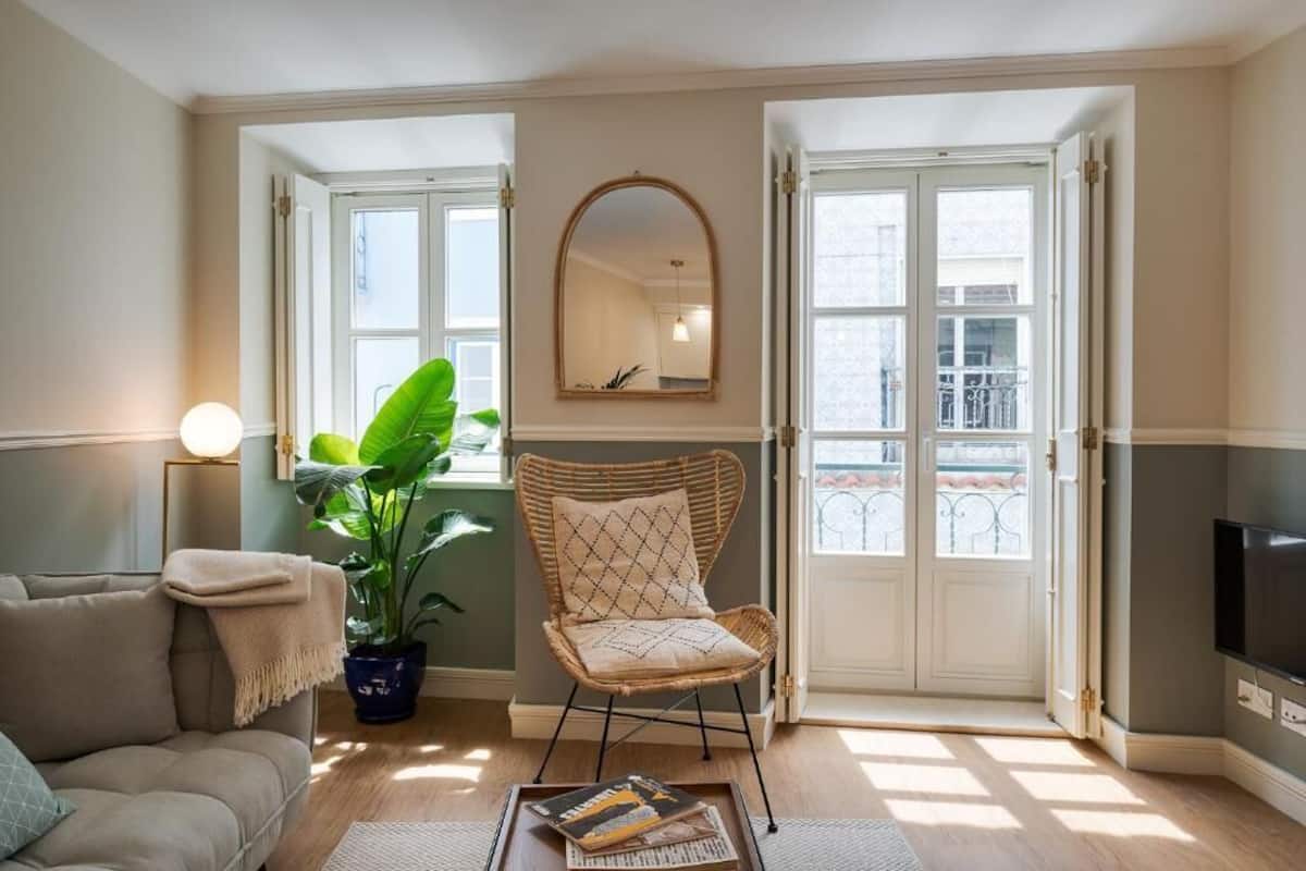 Un salon avec un canapé, un fauteuil, une grande plante, un miroir et un téléviseur.