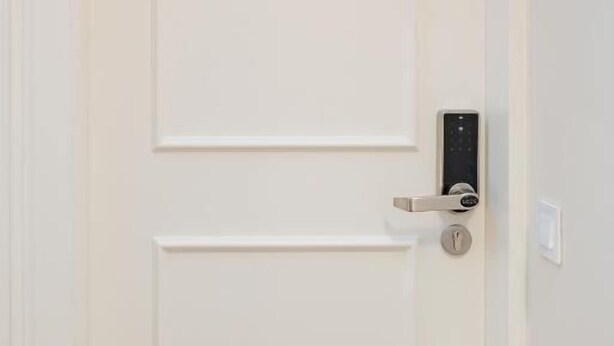 Una puerta blanca con el número 2, un moderno sistema de cierre electrónico y una pequeña ventana en la parte superior.