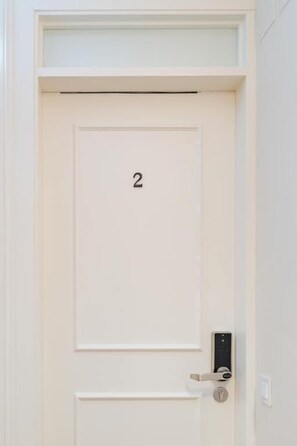 Une porte blanche portant le numéro 2, une serrure électronique moderne et une petite fenêtre située au-dessus de la porte.