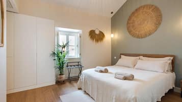 A bedroom with a bed, a potted plant, a window, and a wall-mounted decorative item.