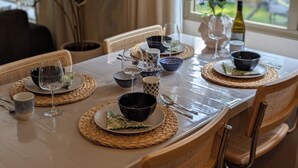 A dining table set with plates, bowls, and wine glasses, surrounded by wicker chairs. - Chalet The Forestbubble #Veluwe #Swimmingpool #Familypark (Voorthuizen)