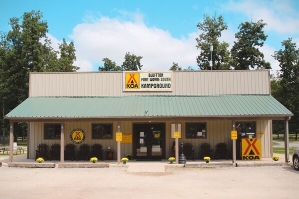 A KOA campground building with a green roof, wooden benches, and yellow flower pots.