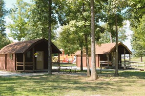 A rustic cabin with a picnic table and benches in a park.