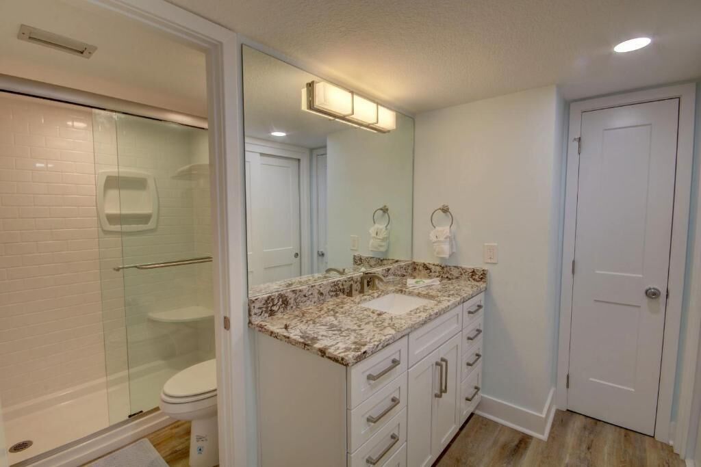 A bathroom with a glass shower enclosure, a sink with a marble countertop, and a white door.