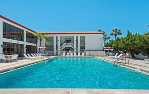 A swimming pool with lounge chairs and umbrellas, a building with a red roof, and palm trees. - El Matador (Fort Walton Beach)