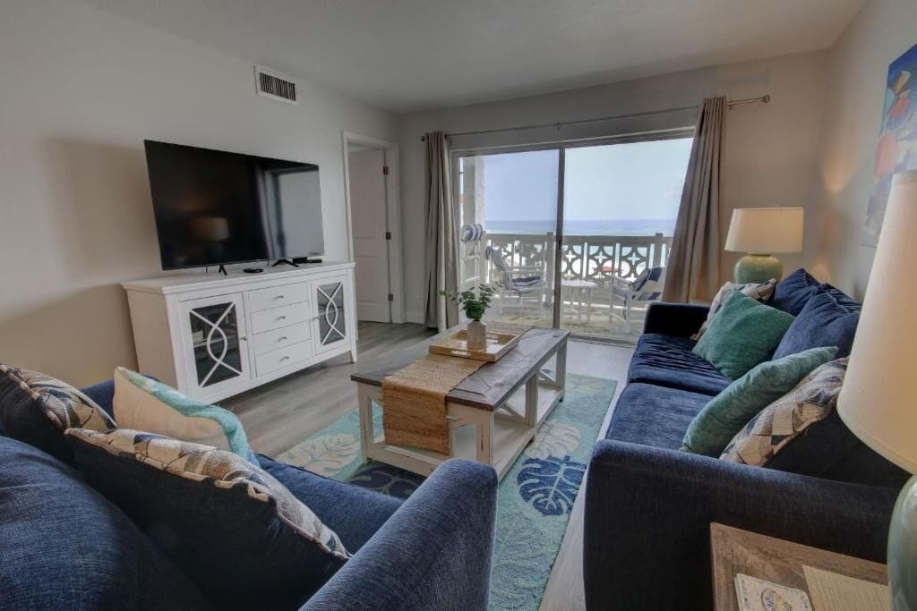 A living room with a TV, a sofa, a coffee table, and a view of the sea through a balcony.