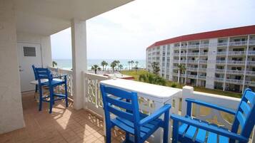 Un balcón con sillas azules y una mesa blanca con vista a una playa y un edificio de hotel.