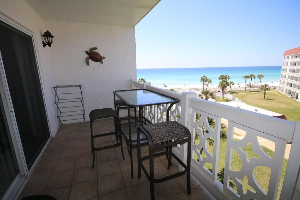 A balcony with a table and chairs, a view of the beach, and a building in the background.