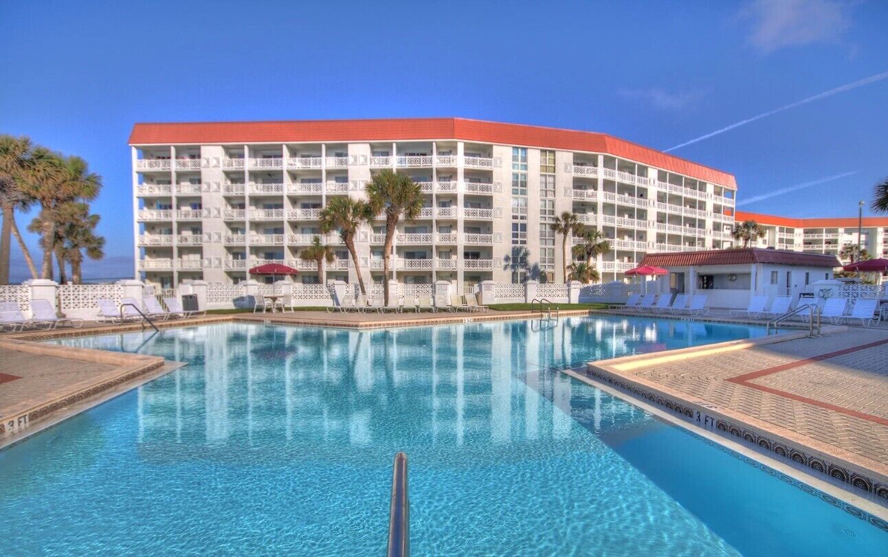 Un hotel con una piscina grande, varios balcones y palmeras.