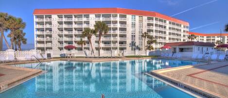 Un hotel con una piscina grande, varios balcones y palmeras.