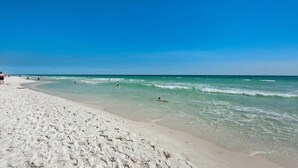 A sandy beach with clear blue water and a few people swimming and walking.