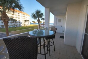 A balcony with a glass table and wicker chairs, overlooking a building with a pool and palm trees. - El Matador (Fort Walton Beach)