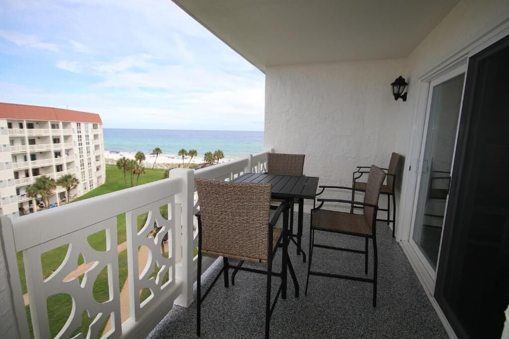 Un balcon avec une table et des chaises, donnant sur une plage et un bâtiment d’hôtel.