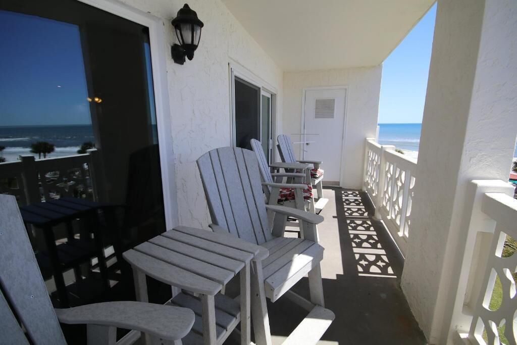Un balcon avec des fauteuils Adirondack, une porte blanche et une vue sur l’océan.