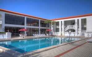A swimming pool with lounge chairs and umbrellas, surrounded by a building with large windows and a red roof. - El Matador (Fort Walton Beach)