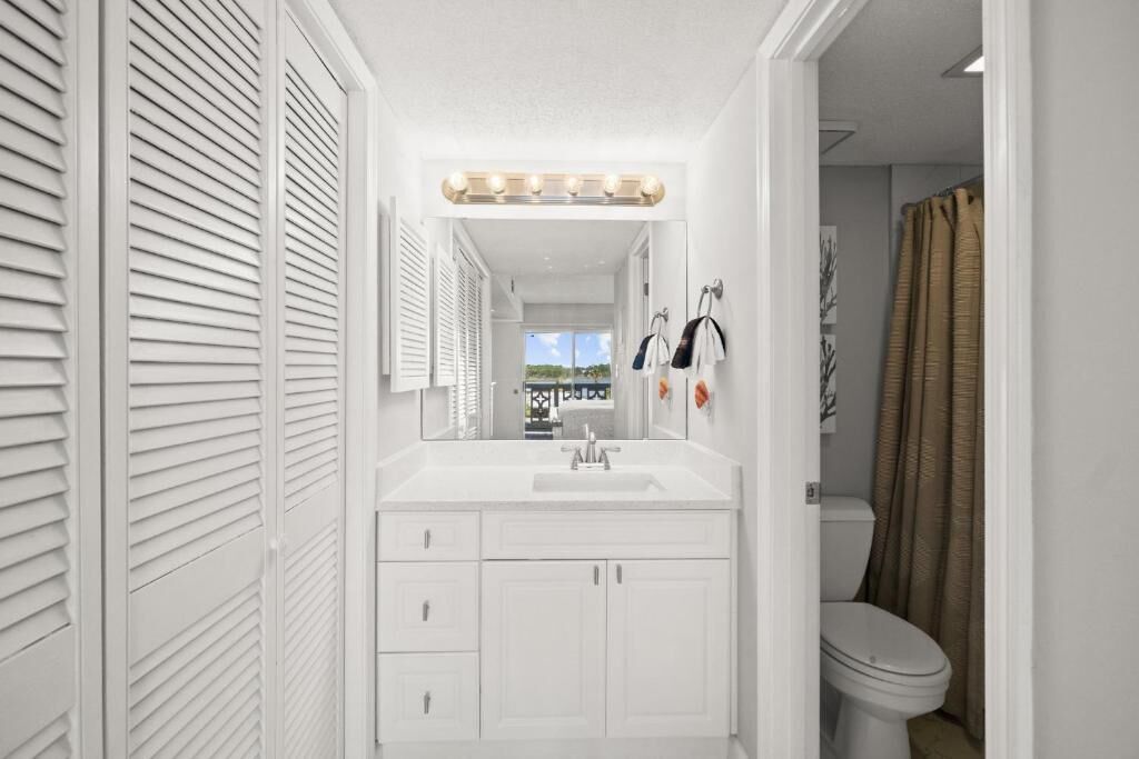 A narrow bathroom with a white vanity, a mirror, and a toilet.