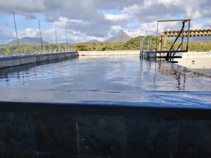 A swimming pool with a view of mountains, a wooden pergola, and a metal ladder.