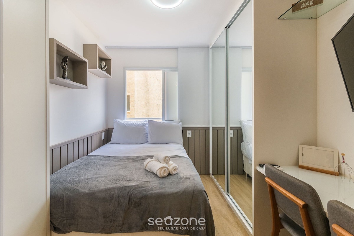 Une chambre à coucher avec un lit, un bureau et une chaise. On y trouve des étagères ornées d’objets décoratifs et une fenêtre.