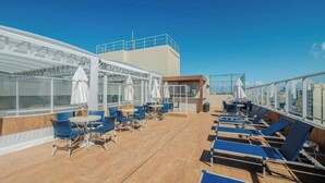 A sun deck with lounge chairs and umbrellas, a covered seating area, and a view of the city skyline. - Condo. w/ Pool and Gym 70 m From the Beach - SMA (Salvador)