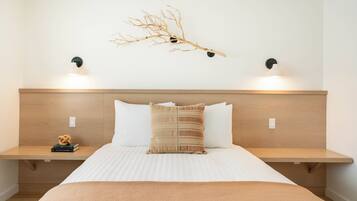 A hotel room with a wooden headboard, two bedside tables, a bed with white bedding, a textured throw blanket, and wall-mounted lighting.