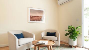 A room with two armchairs, a small wooden table with a book, a large potted plant, and a framed picture on the wall.