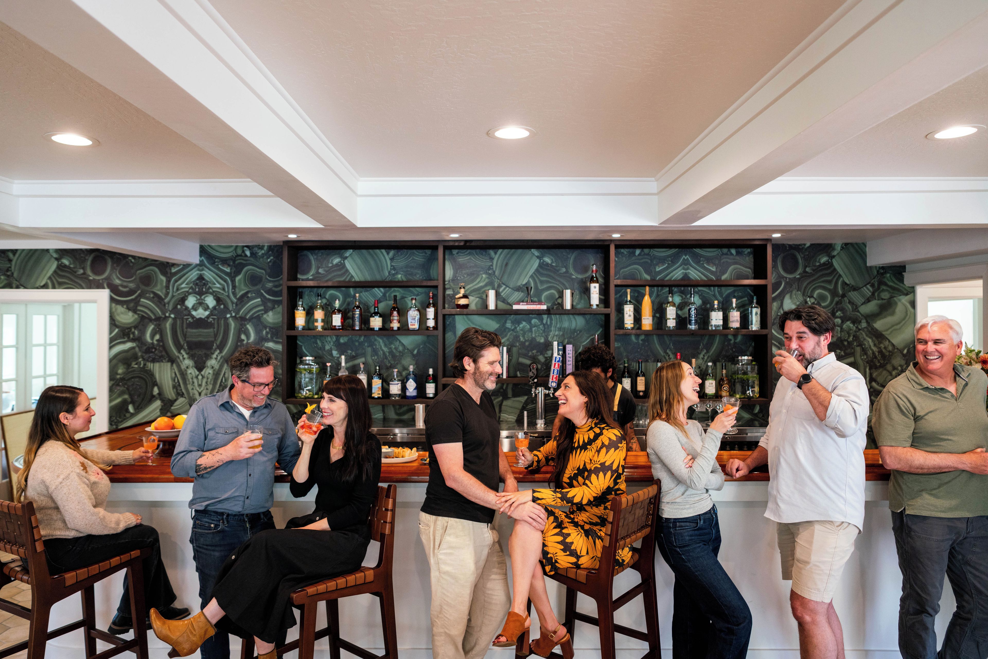 A group of people in a bar area with a high ceiling and recessed lighting.