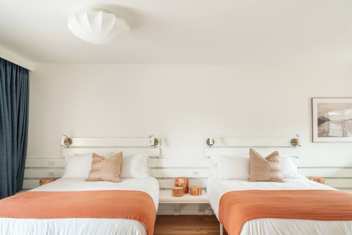 A hotel room with two beds, white bedding, and a wooden headboard.