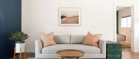 A living room with a grey sofa, a round wooden coffee table, a framed picture on the wall, and a green trunk.