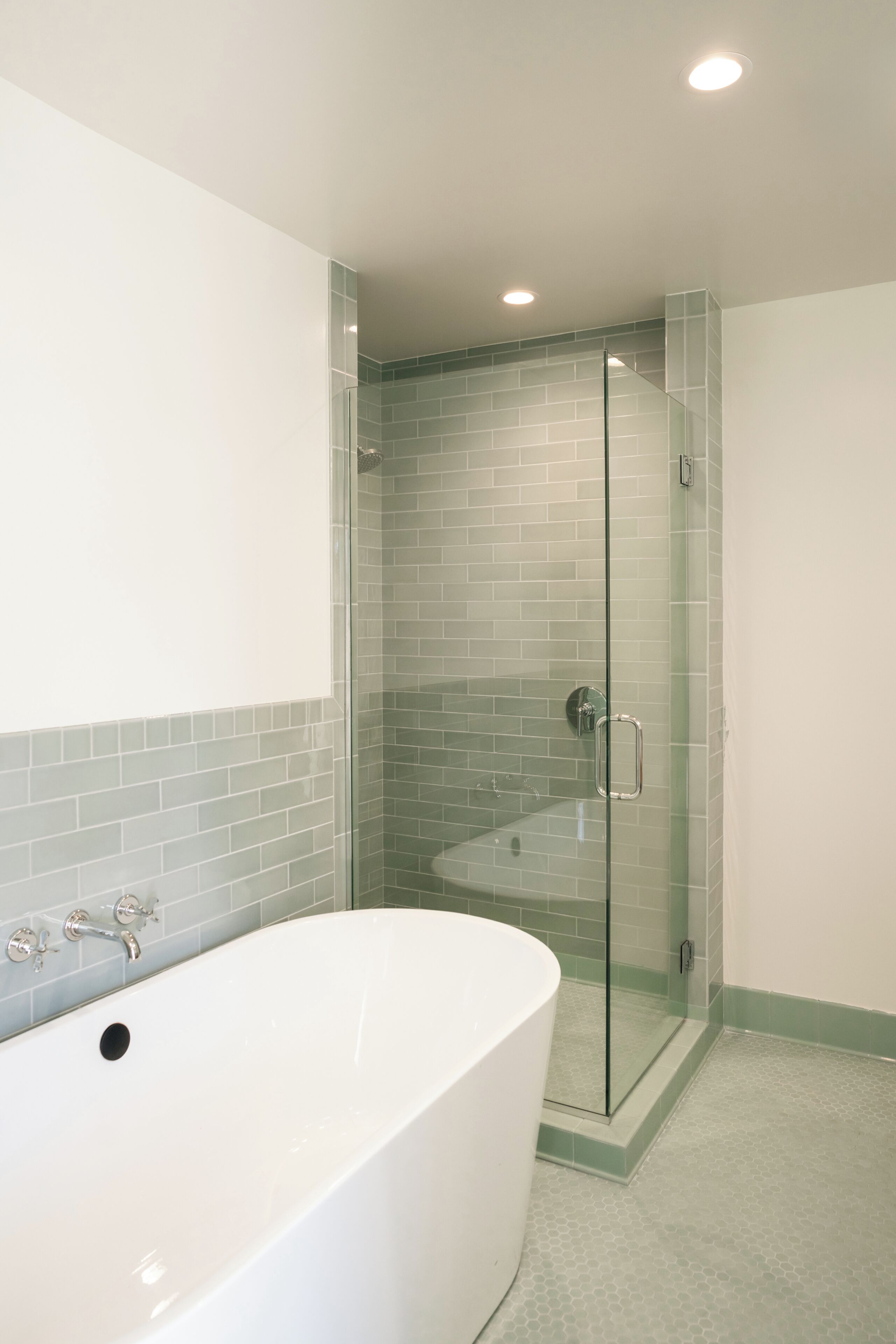 A bathroom with a glass-enclosed shower, a white bathtub, and a tiled floor.