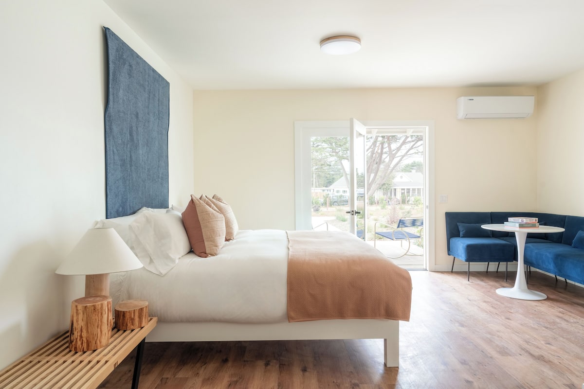 A modern bedroom with a bed, bedside table, and a view of the outdoors.