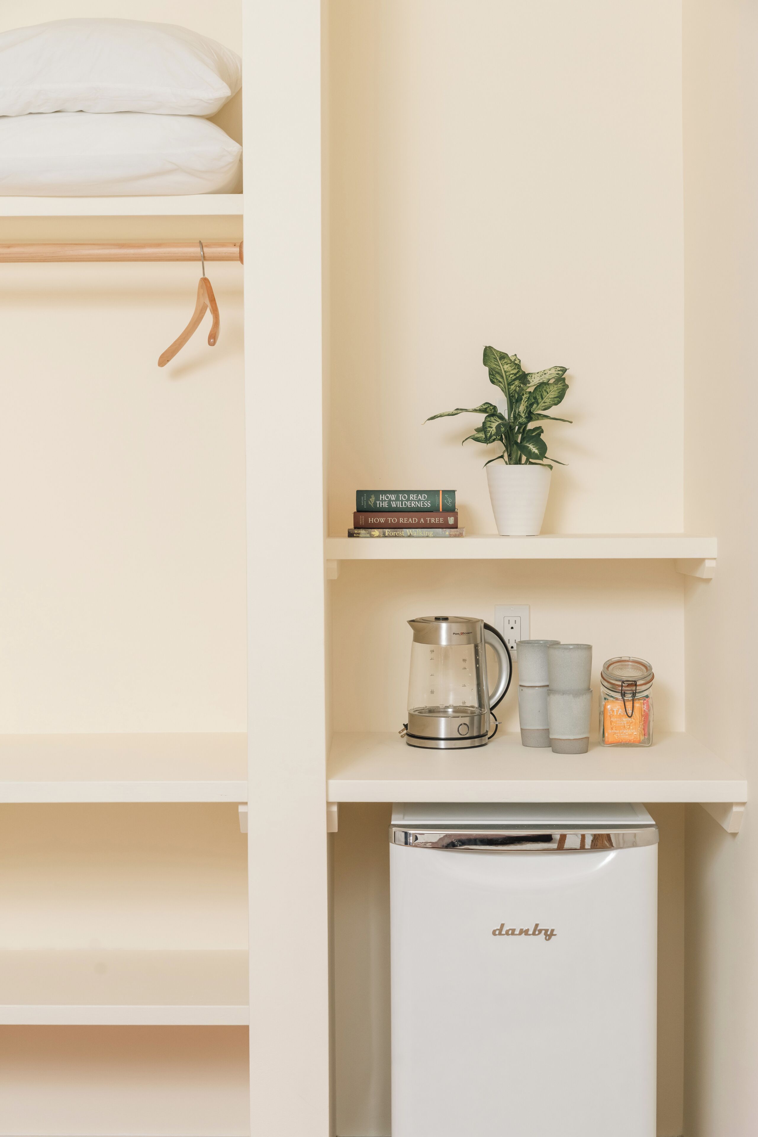 Prateleira branca com uma planta, livros, cafeteira e um refrigerador Danby.