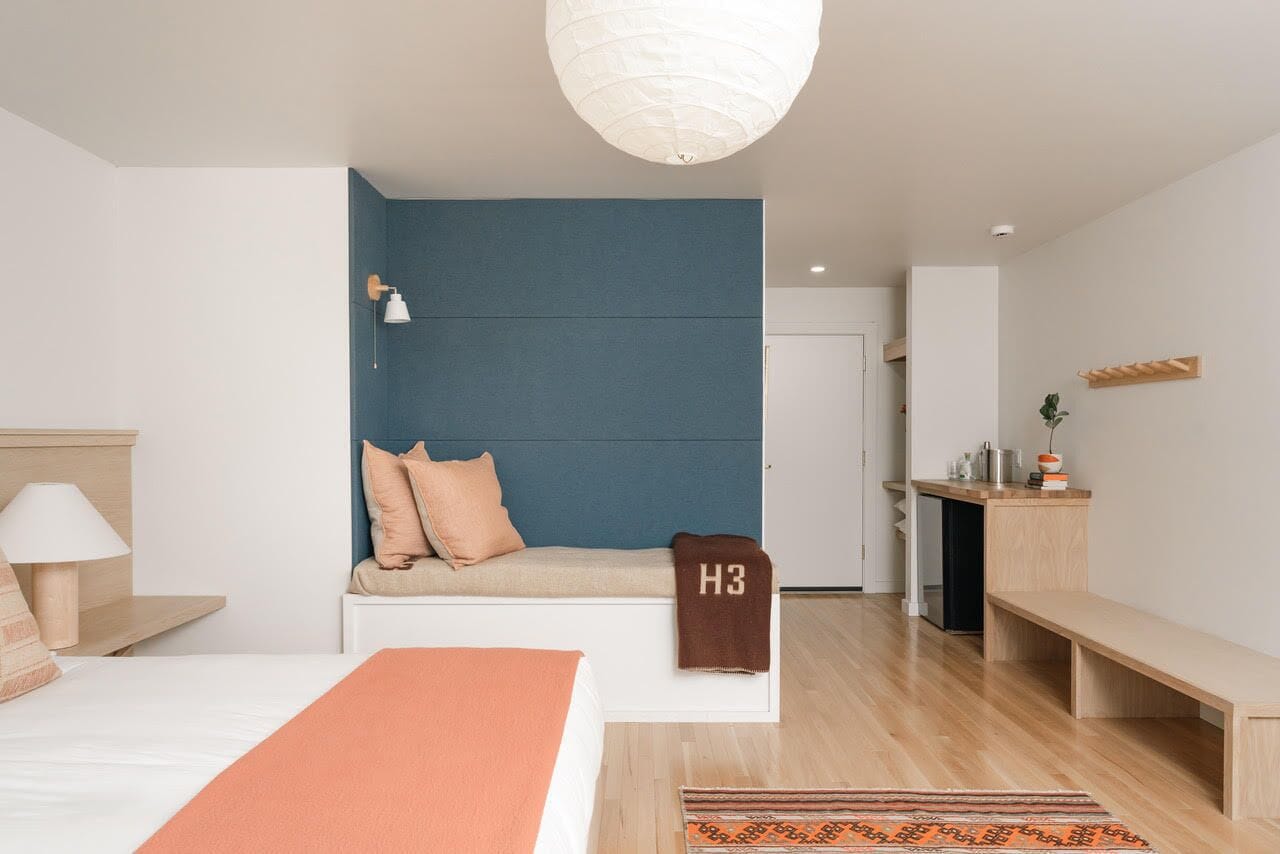 Una habitación de hotel moderna con una cama, un banco, un escritorio y una lámpara colgante.