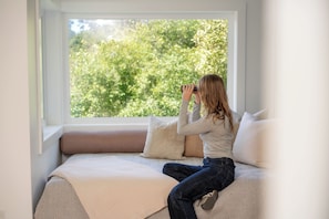 A person sitting on a bed with a window view of trees. - Mendocino Cove (Fort Bragg)