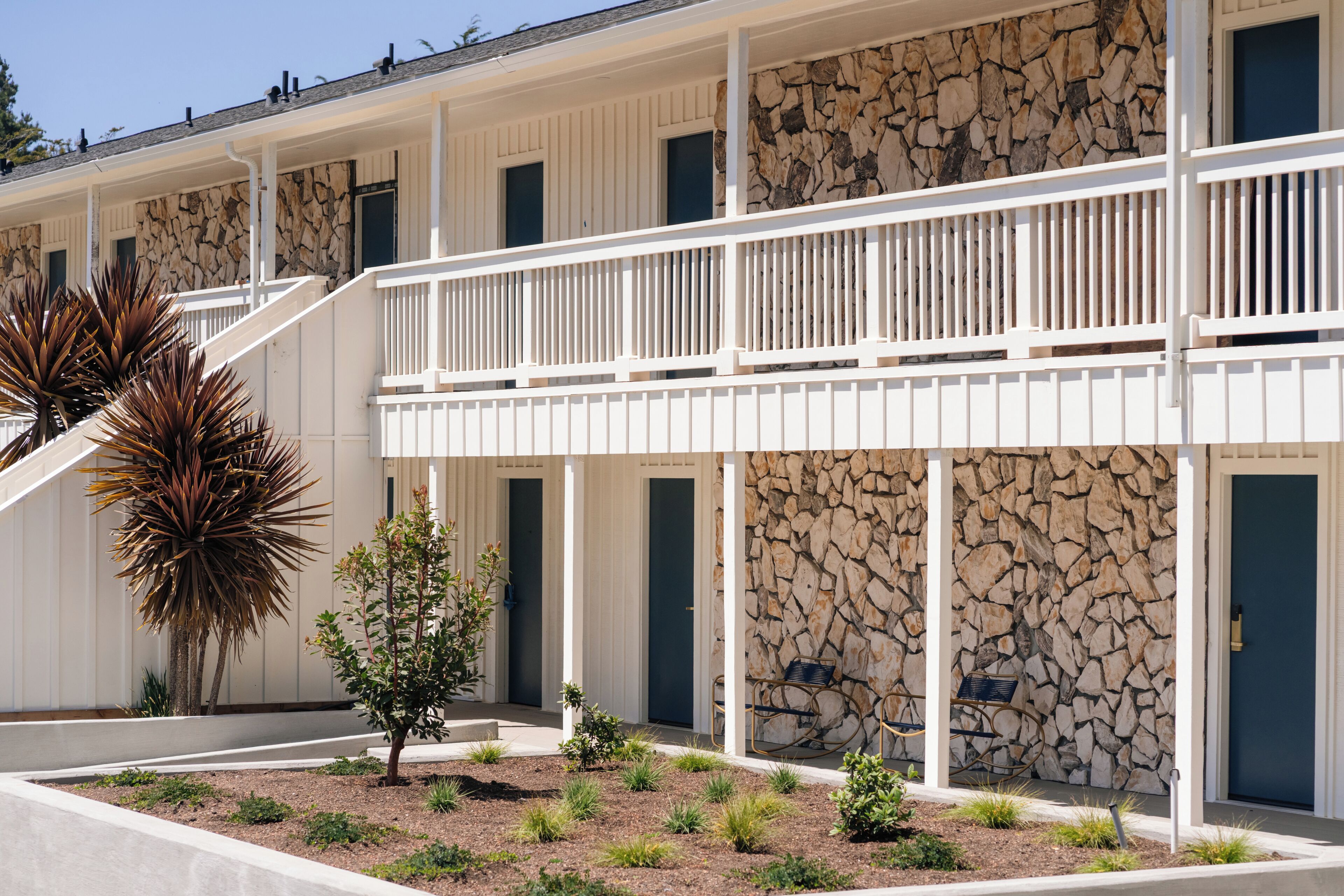 A hotel with a stone facade, white balconies, and a landscaped garden with desert plants.
