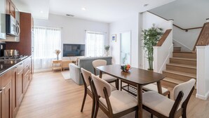 A modern kitchen with wooden cabinets and a built-in microwave. There is a dining area with a table and chairs, and a staircase leading to another level.
