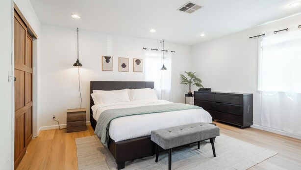 A bedroom with a bed, bedside tables, a bench, a dresser, and a plant.