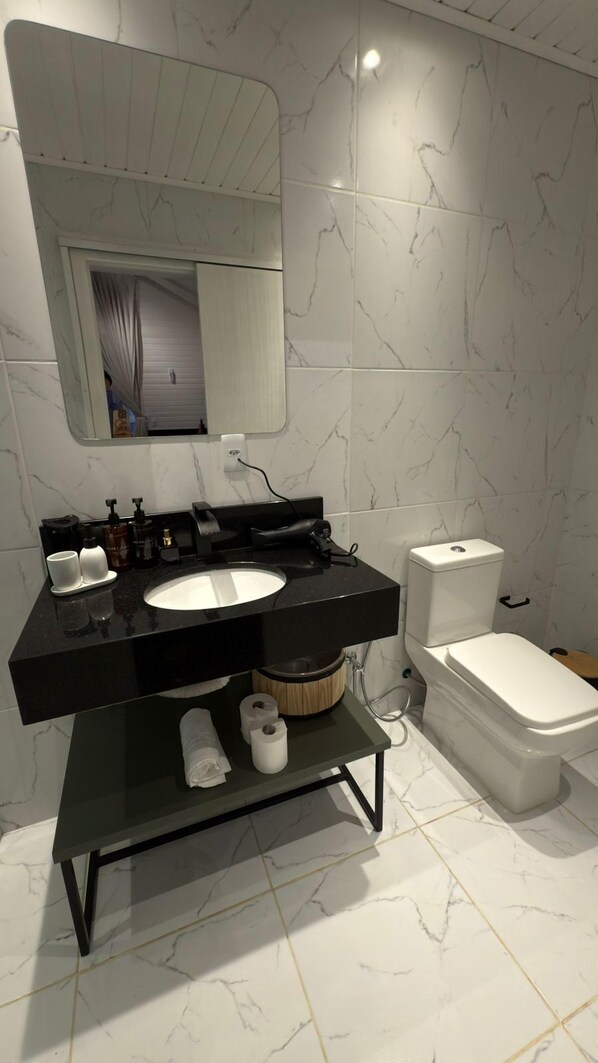 A modern bathroom with a black vanity, white marble tiles, a toilet, and a shower area. - Chalé Carmenere - Vila Chamonix (Urubici)