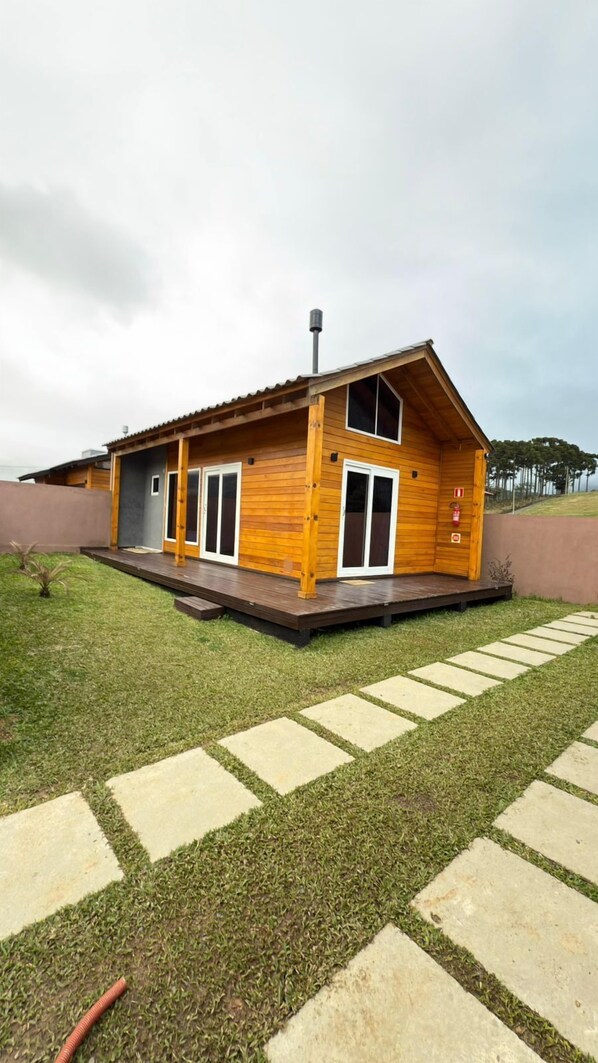 A wooden cabin with a sloped roof, large windows, and a small deck. - Chalé Carmenere - Vila Chamonix (Urubici)