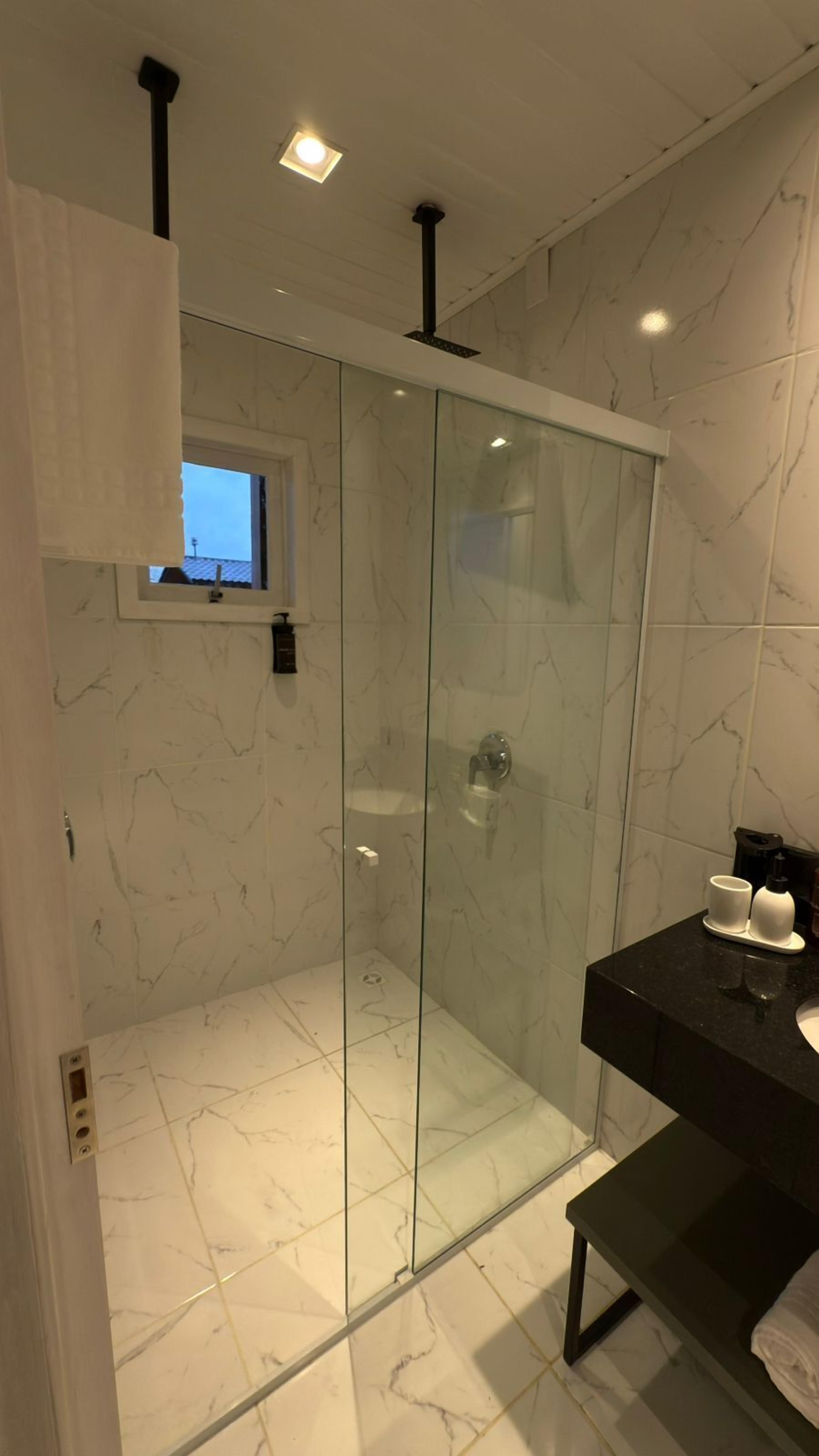 Un baño moderno con ducha envuelta en cristal, baldosas de mármol y encimera negra con lavabo.