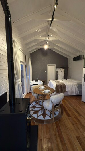 A cozy room with a bed, a small table with chairs, a bathtub, and a heater. - Chalé Carmenere - Vila Chamonix (Urubici)