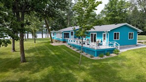 Een blauw huis met twee verdiepingen en een terras, omgeven door een verzorgd gazon en bomen.