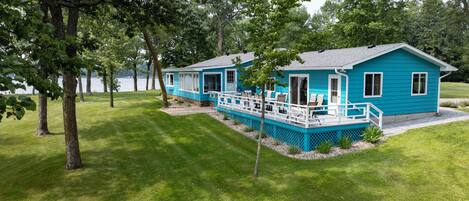 Een blauw huis met twee verdiepingen en een terras, omgeven door een verzorgd gazon en bomen.