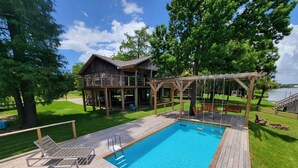Una terrazza in legno con piscina, poltrone relax e una casetta in legno con veranda e altalena.