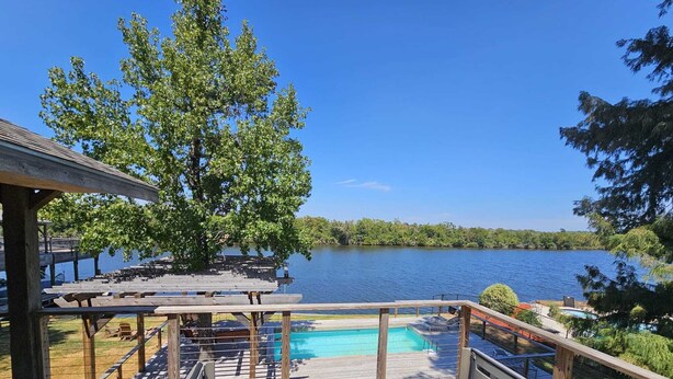 Un terrazzo in legno con idromassaggio, piscina e tavoli da picnic con vista su un lago.