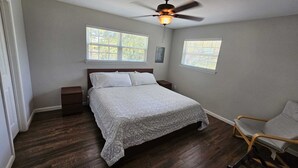 Una camera da letto con un letto, due comodini, una ventola a soffitto, due finestre e una sedia.