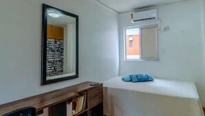 Un dormitorio con cama, mesita de noche, espejo y equipo de aire acondicionado.