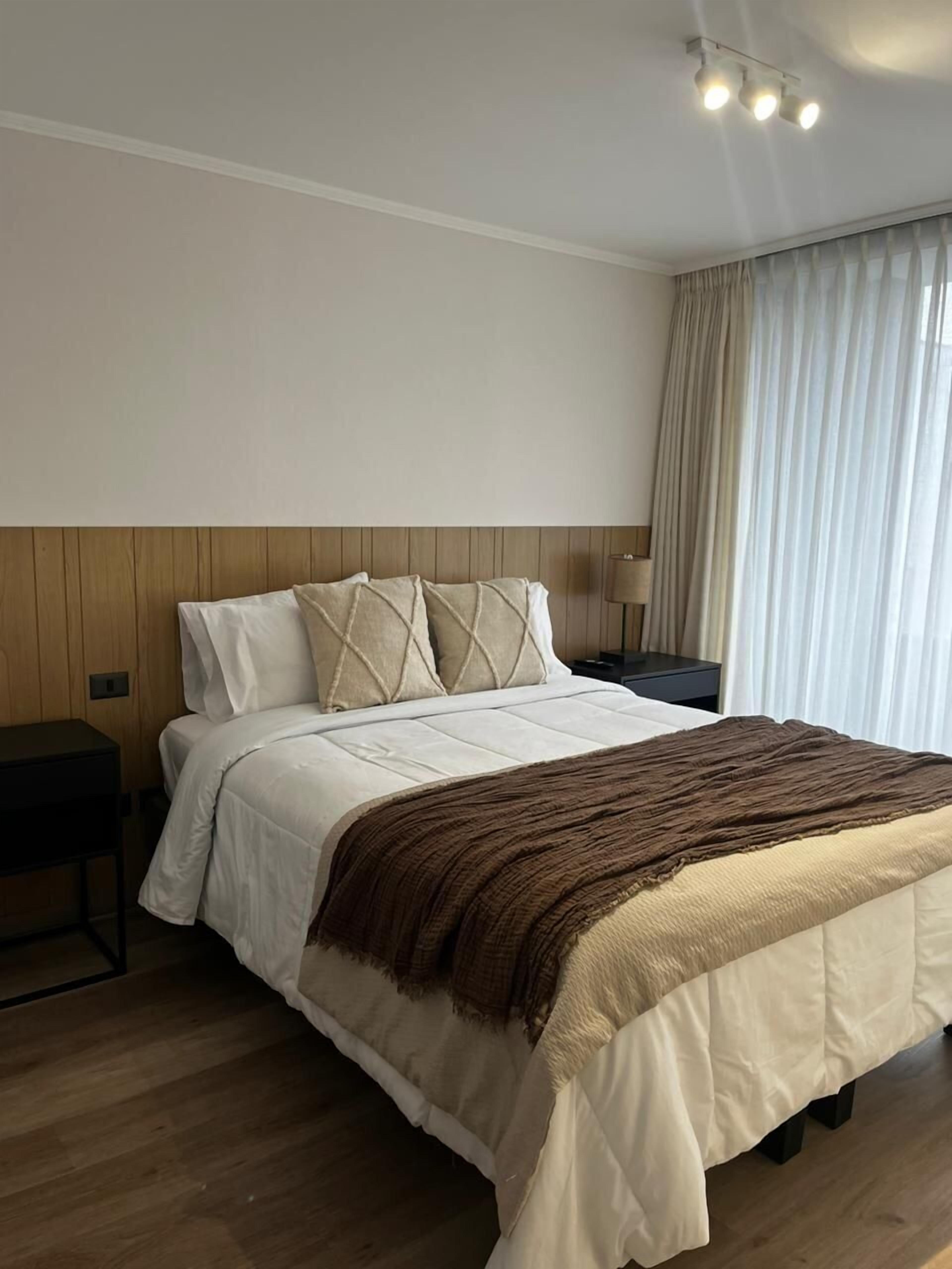 A neatly made bed with a white and brown blanket, a wooden headboard, and a bedside table with a lamp.