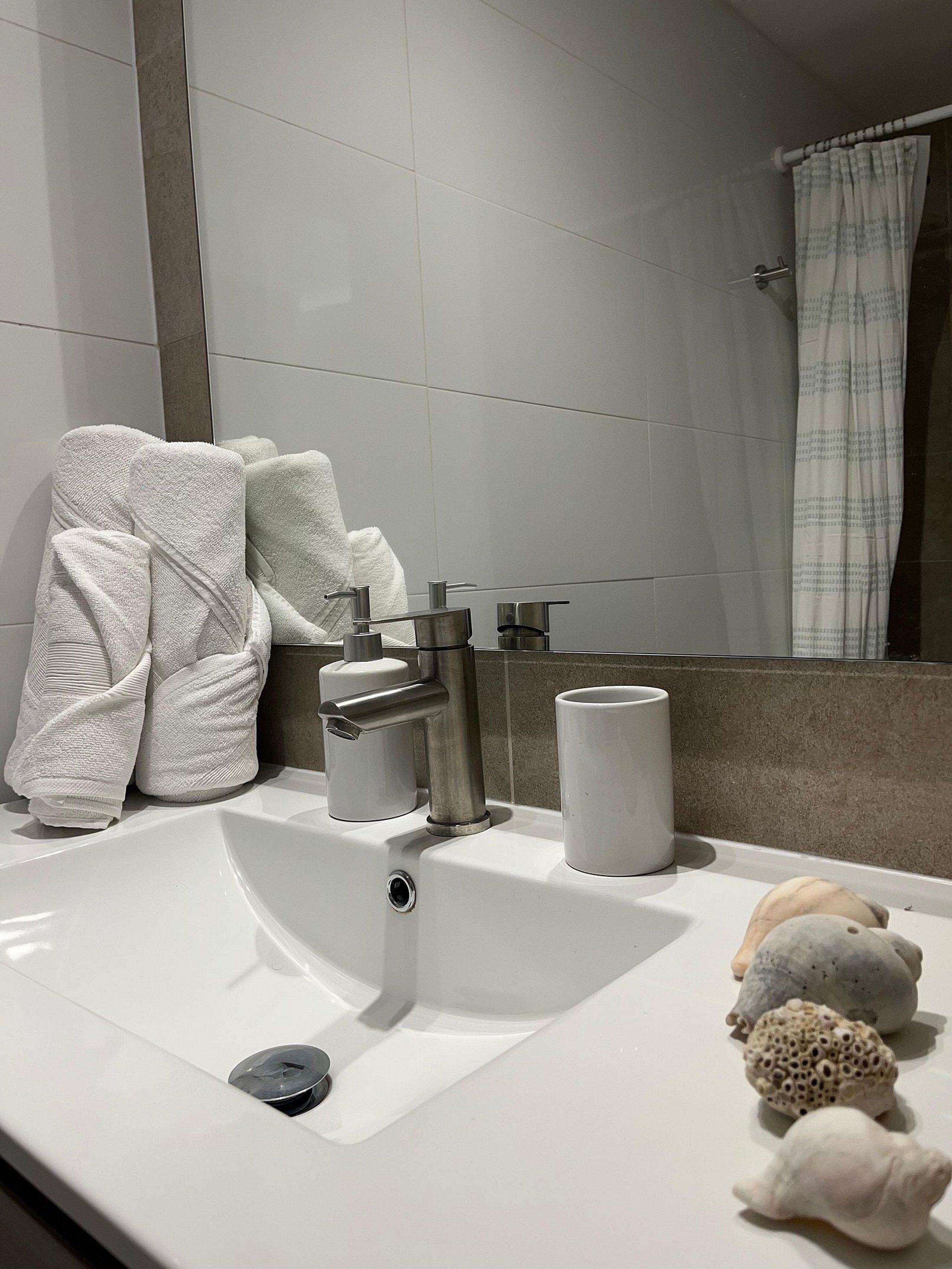 Un baño moderno con un lavamanos blanco, dos grifos, un espejo y una cortina de ducha.