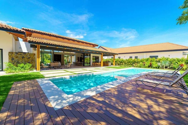 Une maison moderne dotée d’une piscine, d’un patio et d’un espace extérieur aménagé et couvert.
